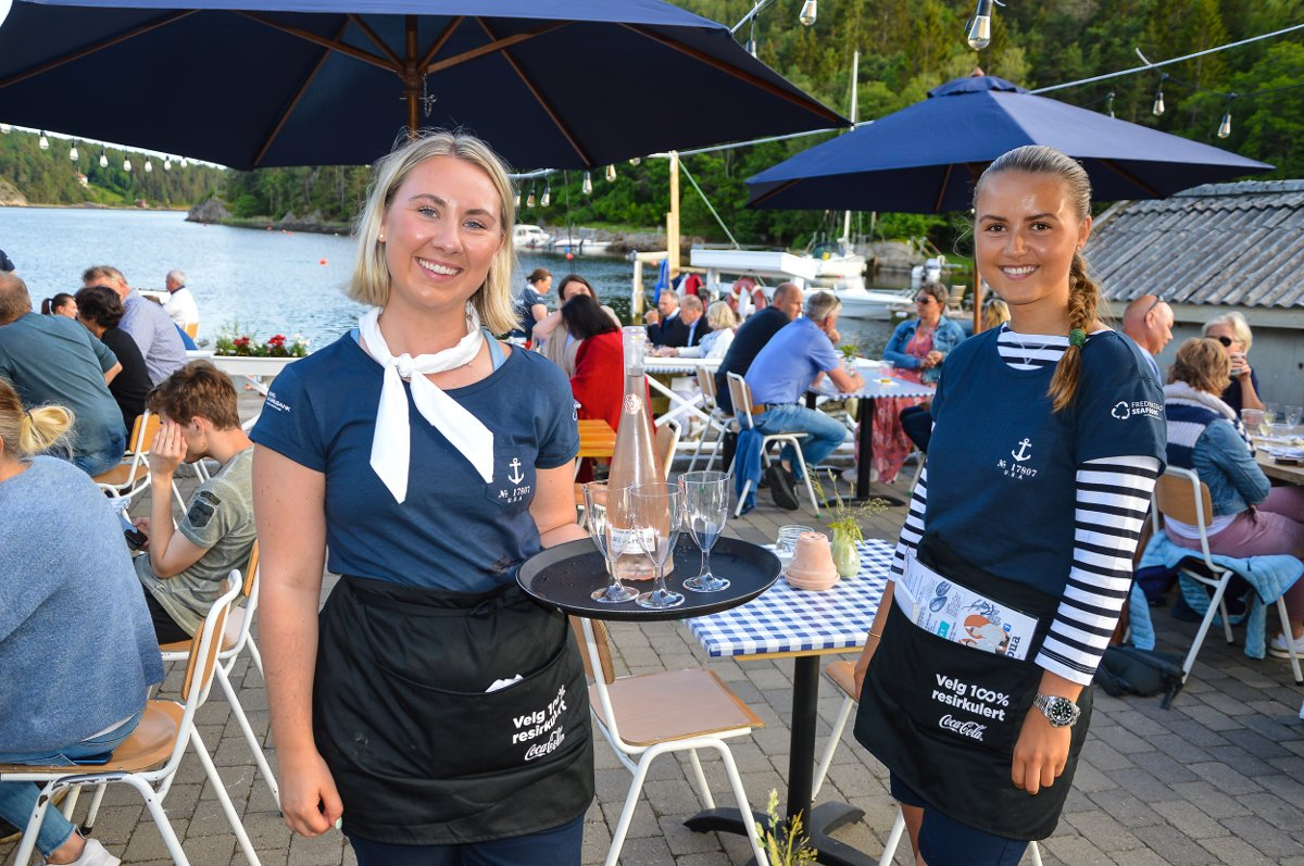 To smilende servitører i Sjøbua-uniform klar til å servere gjester på terrassen – profesjonell service ved Ringdalsfjorden i Sponvika