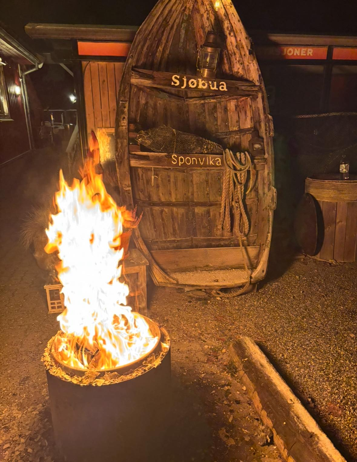 Koselig bål foran den ikoniske gamle båten med 'Sjøbua Sponvika'-skilt – unik atmosfære ved restauranten nær Halden