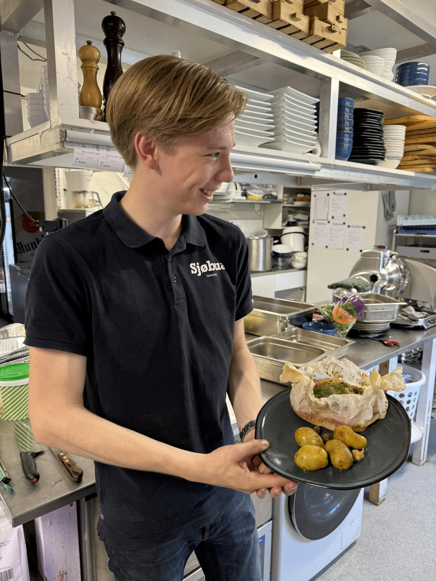 Ung kokk i Sjøbua-uniform serverer ovnsbakt fisk med nypoteter – fersk norsk sjømat fra Ringdalsfjorden ved Sponvika