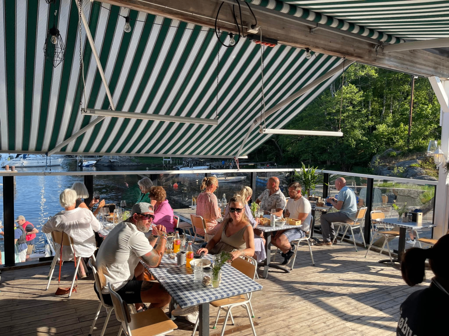 Fornøyde gjester nyter sjømat på terrassen ved Sjøbua i Sponvika – livlig sommerkveld med utsikt over Ringdalsfjorden nær Halden